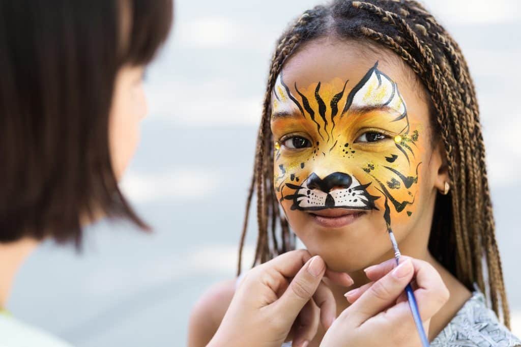 Little girl getting her face painted by face painting artist.
